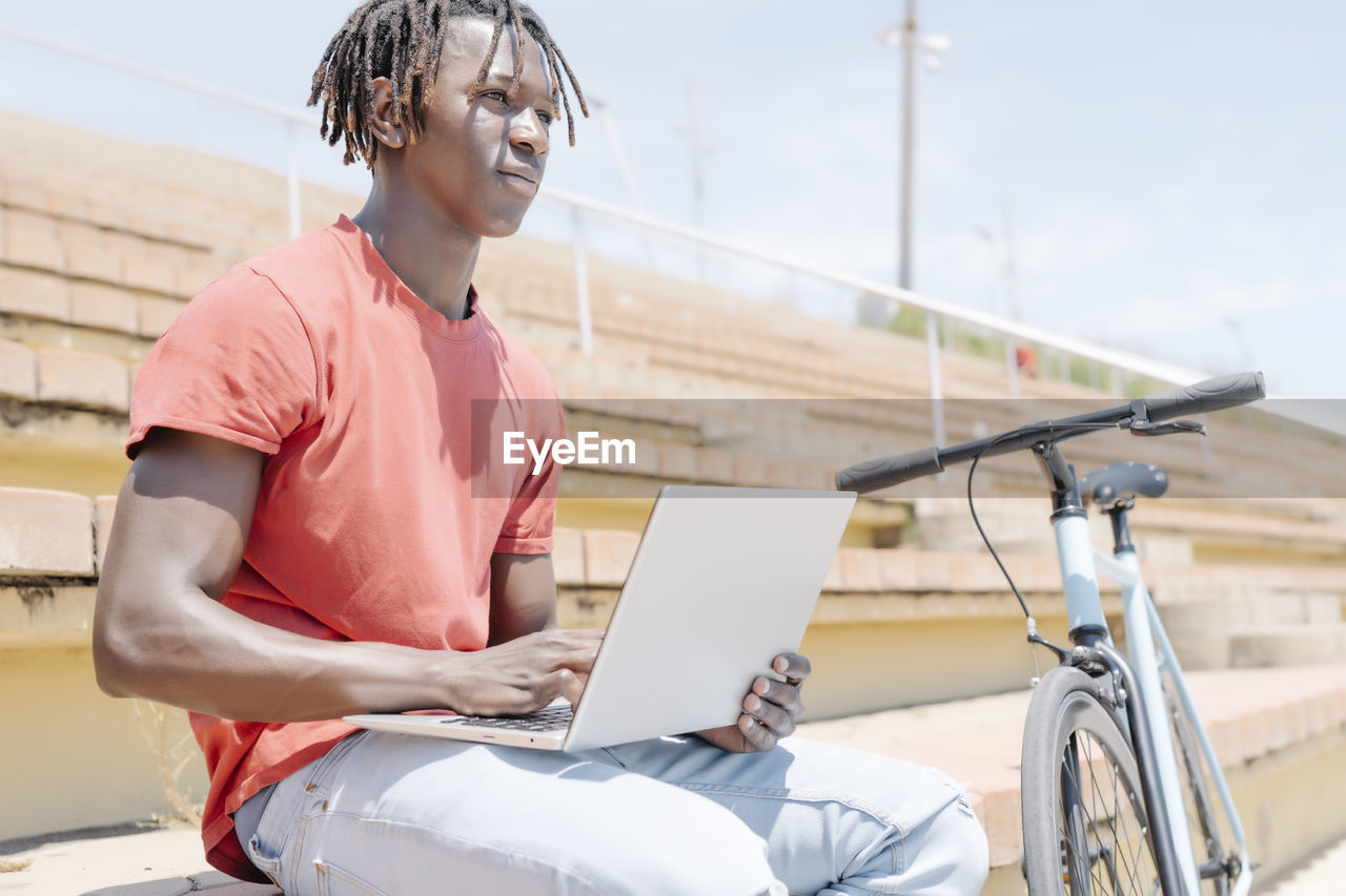 Ethnic guy using laptop near bicycle