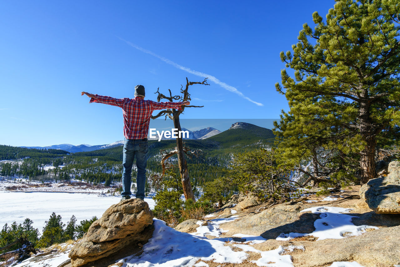 Rear view of man standing on rock against mountains during winter