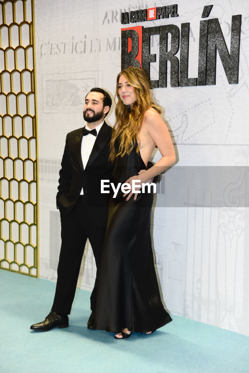 adult, two people, women, men, full length, love, young adult, togetherness, portrait, fashion, emotion, clothing, positive emotion, looking at camera, standing, smiling, female, happiness, dress, indoors, romance, elegance, formal wear, event, business