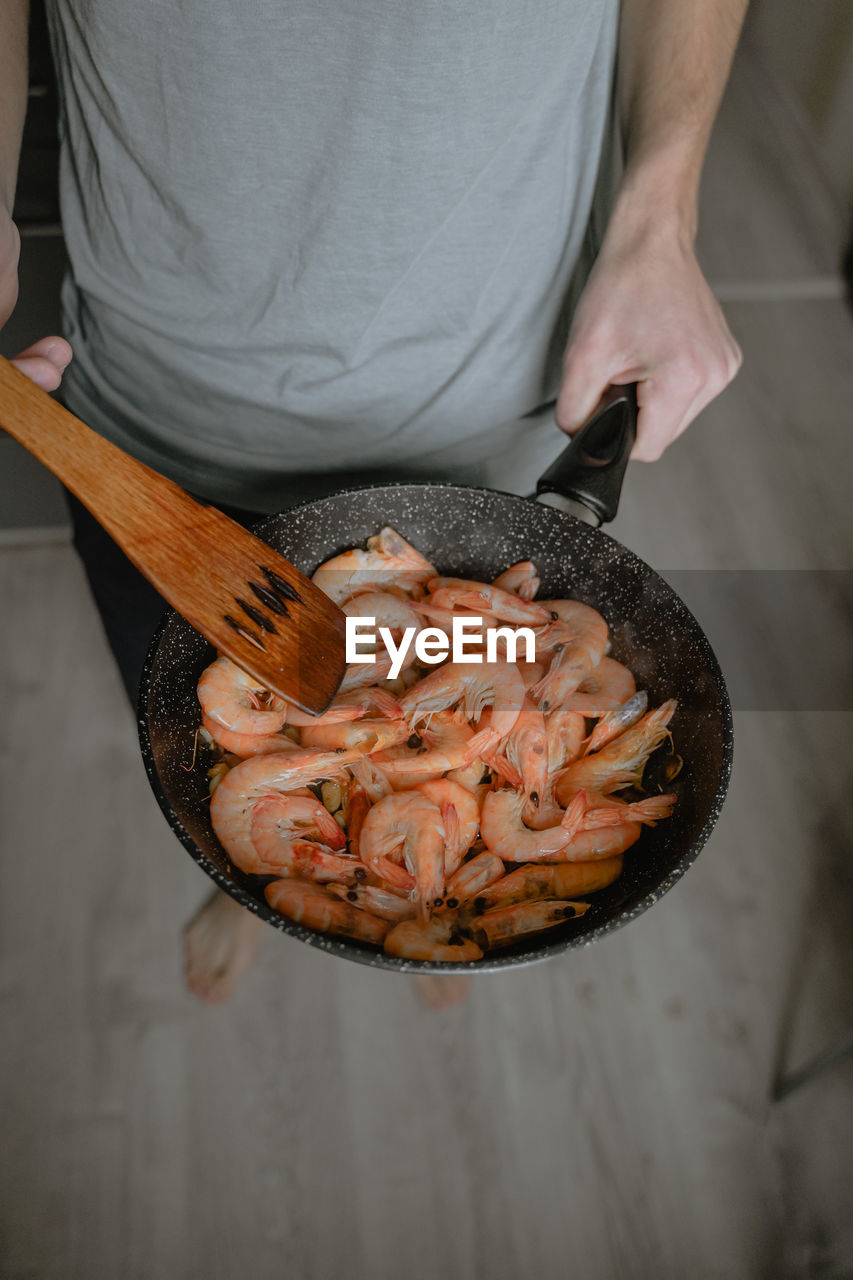 Cooking shrimp at home, fried in a pan, holding, large fresh shrimp in a pan