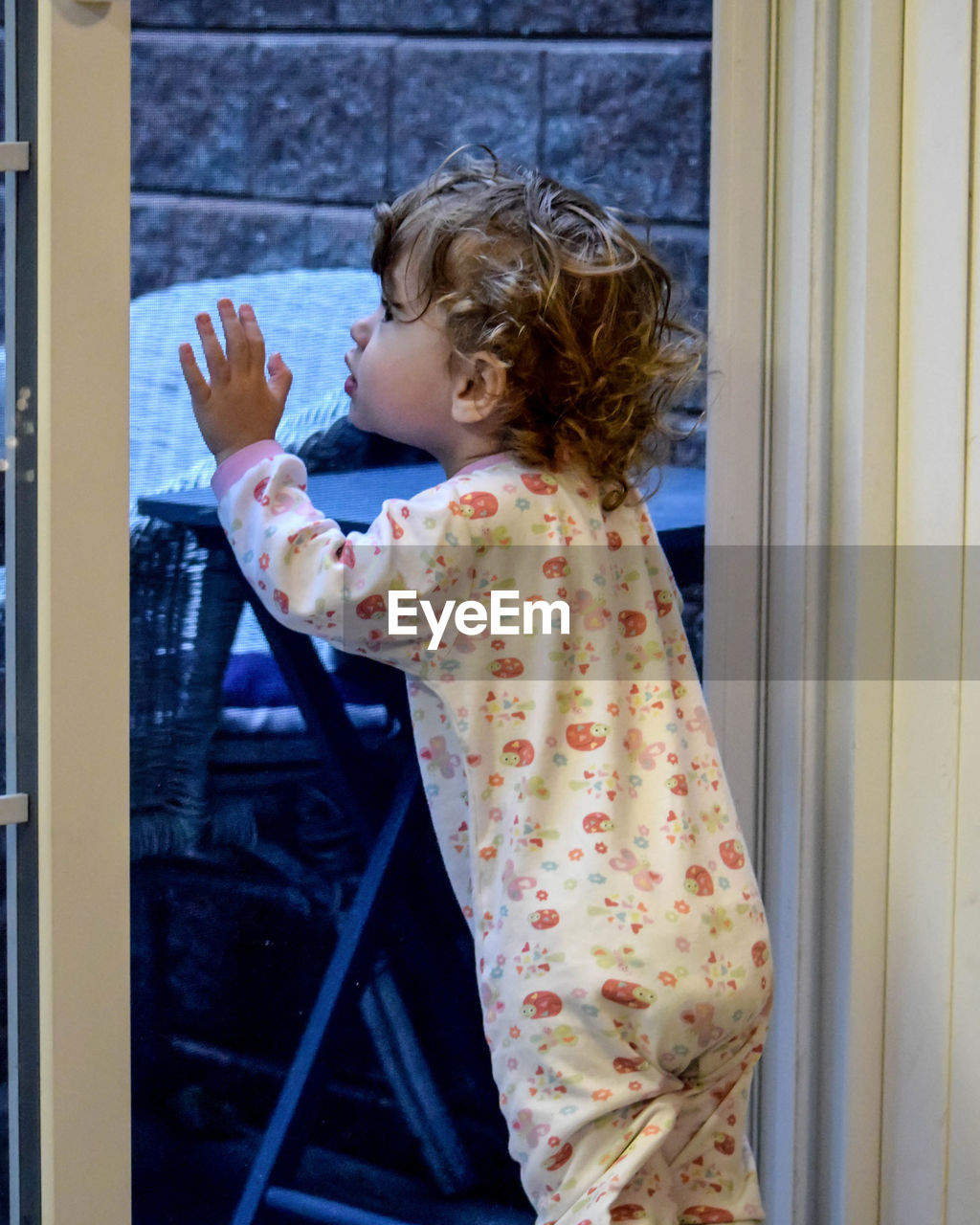 Baby girl looking through glass door at home