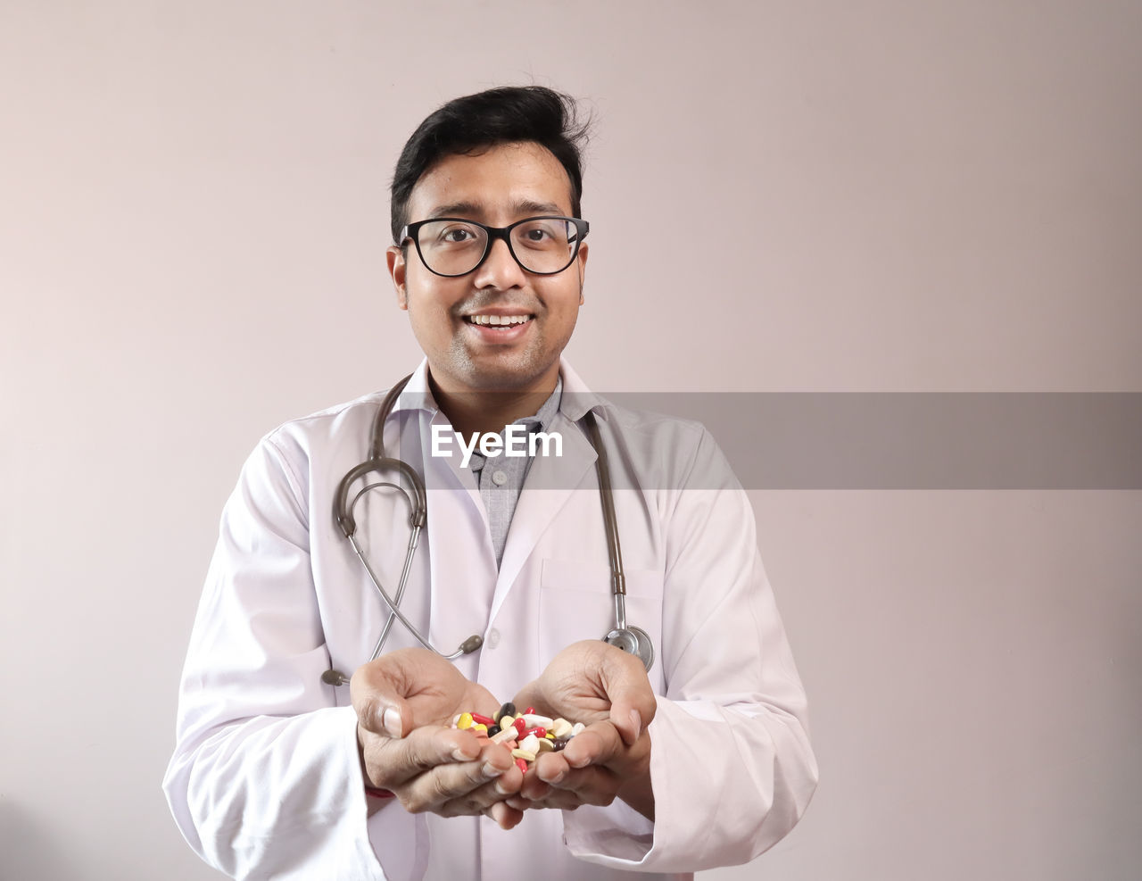Portrait of smiling doctor holding capsules while standing against beige background