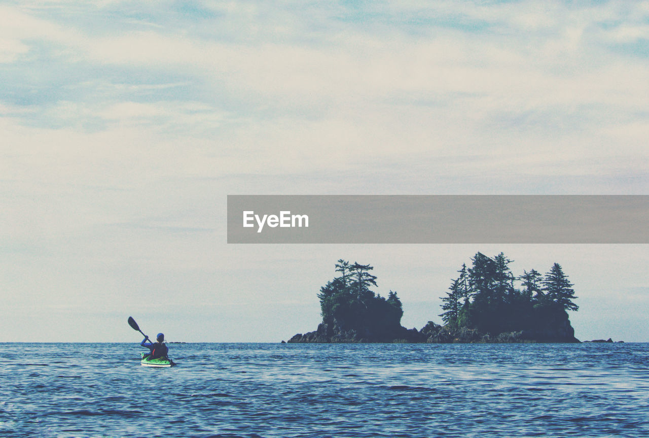 Rear view of man kayaking in sea against sky