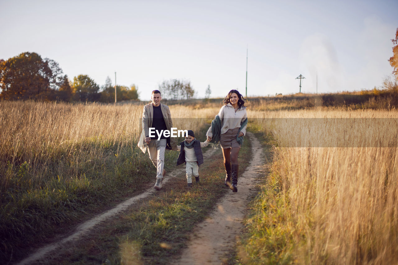 Stylish family with a boy child on a field in the dry grass in autumn