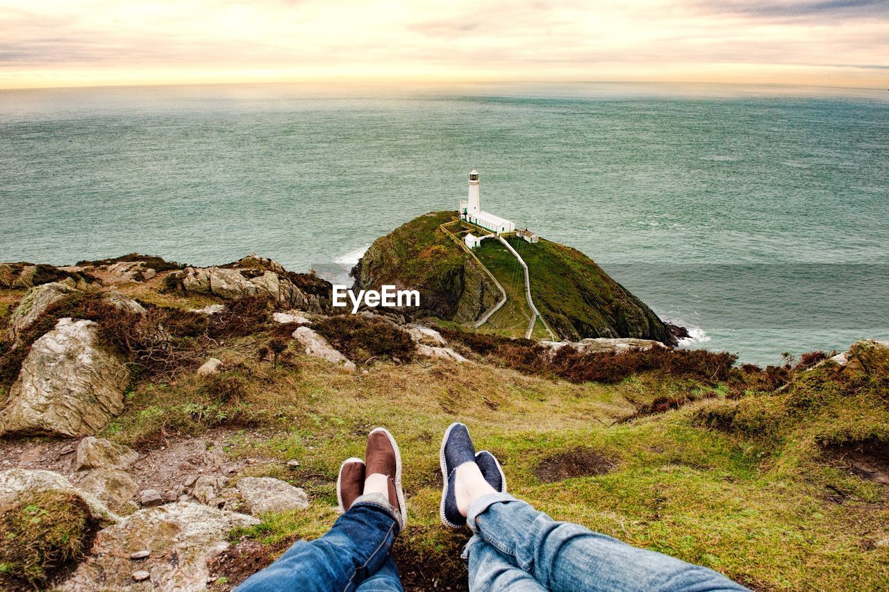 Low section of people on cliff by sea against sky