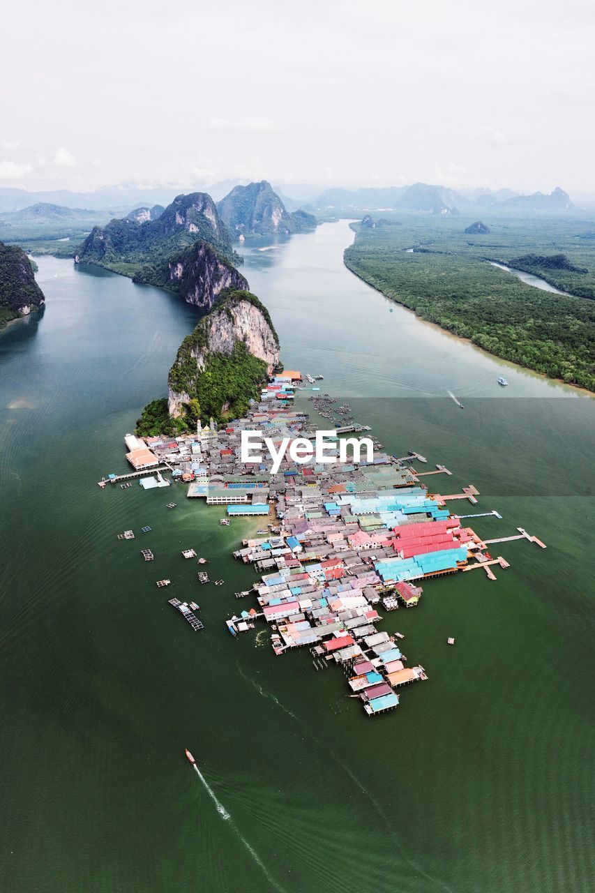 High angle view of fishing village on sea by mountains against sky