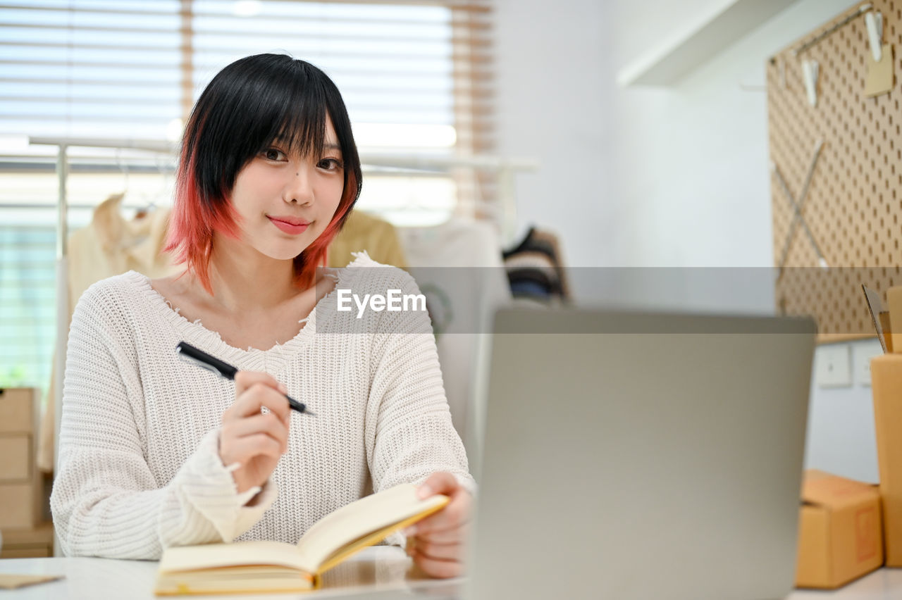 portrait of young woman using laptop while sitting on sofa at home