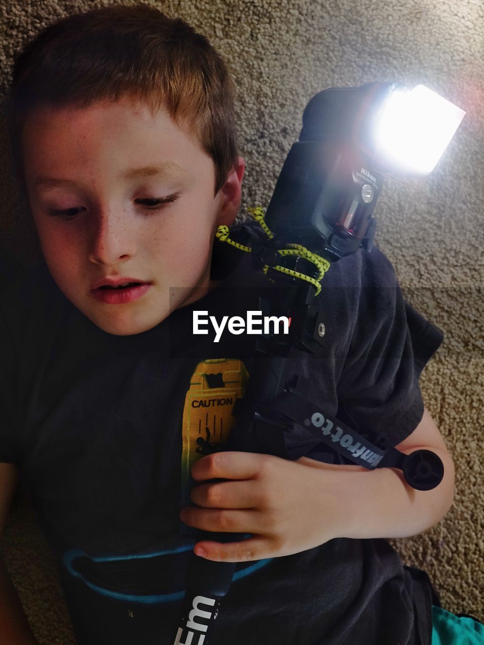 Cute boy holding camera with illuminated flashlight against wall