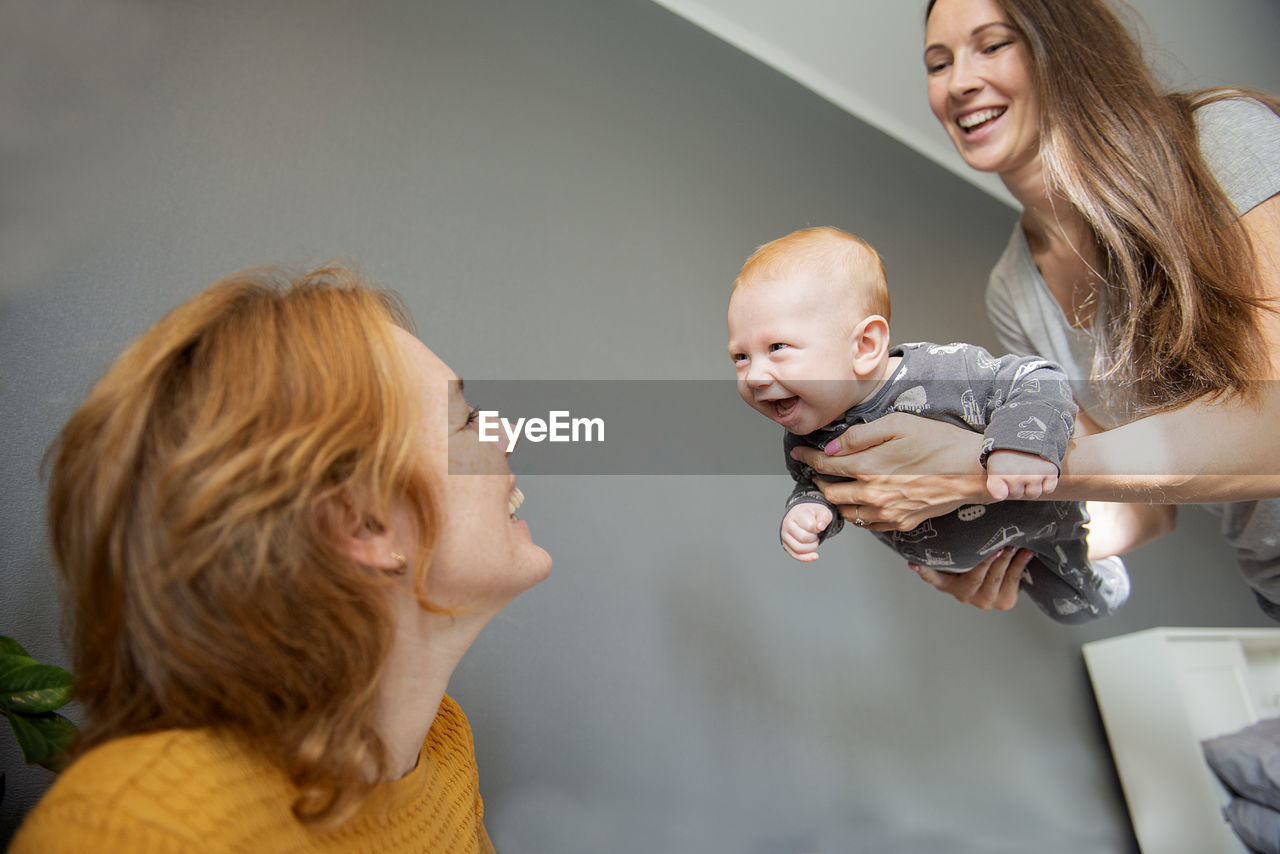 Grandmother and mother in living room playing with smiling newborn baby boy