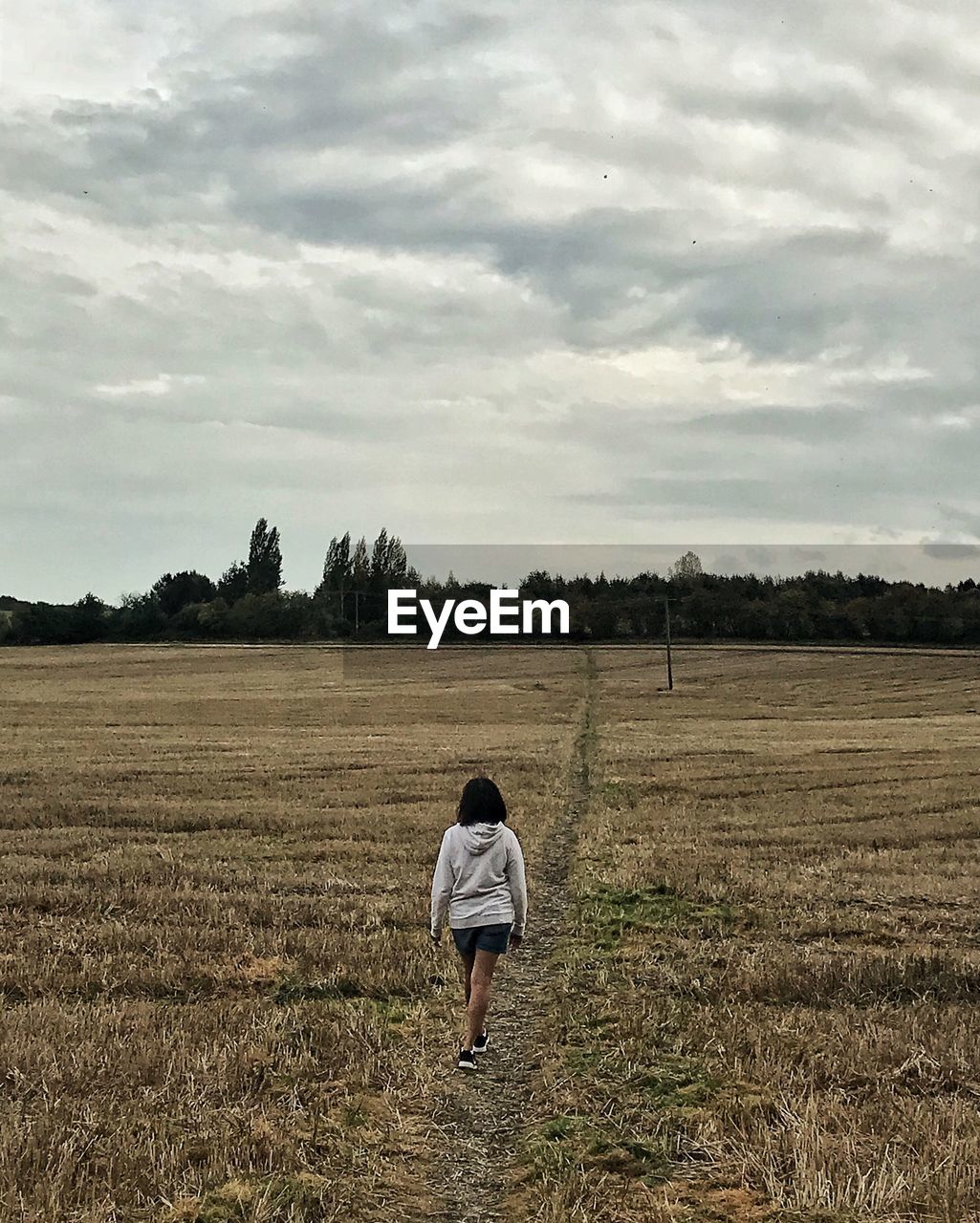 Rear view of woman walking on field against sky