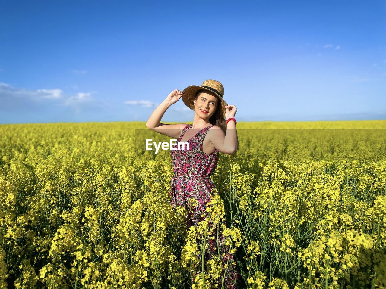Happy woman wearing dress and hat in a field of canola flowers on a sunny day
