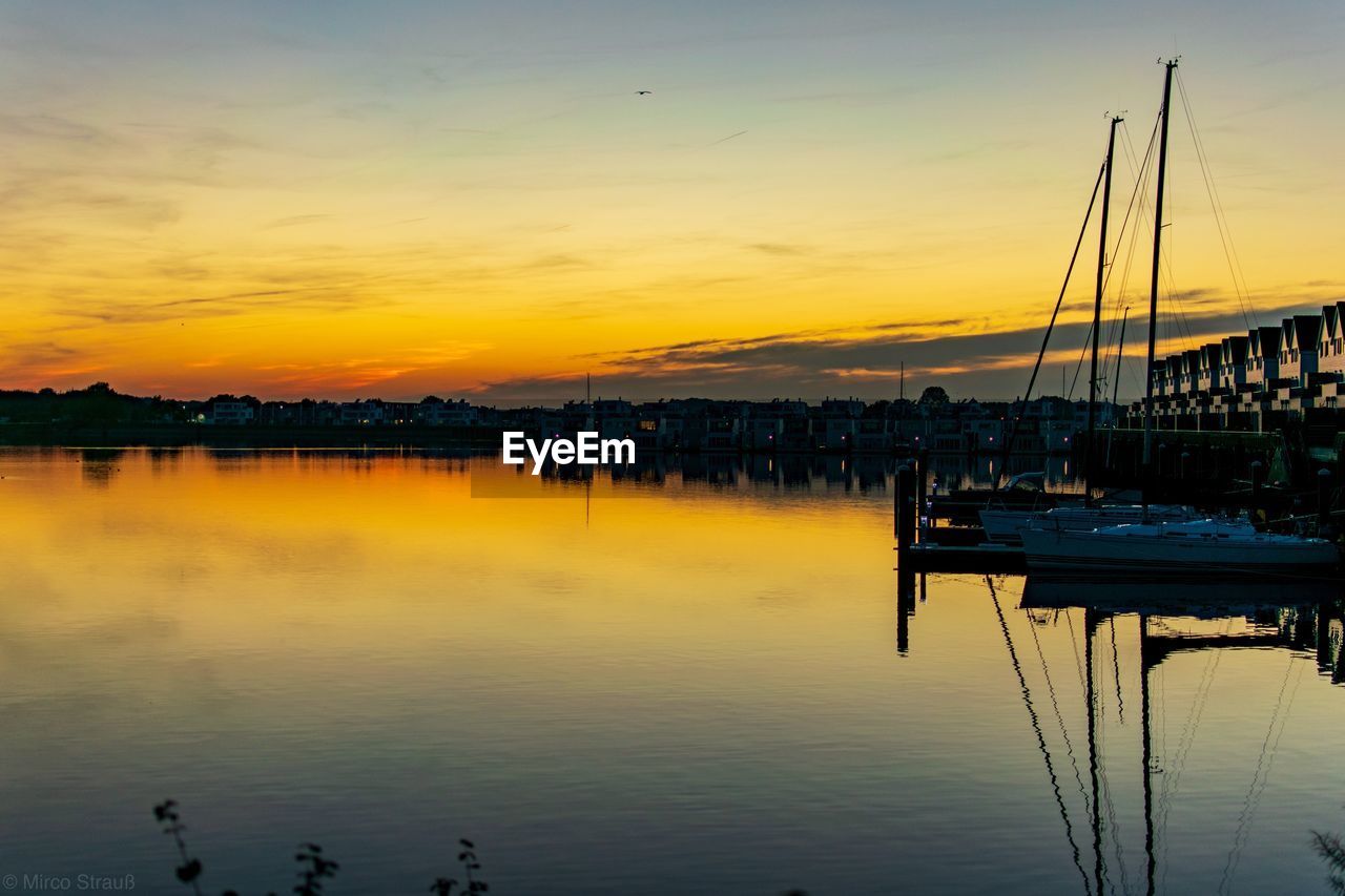 Sailboats moored at harbor against sky during sunset