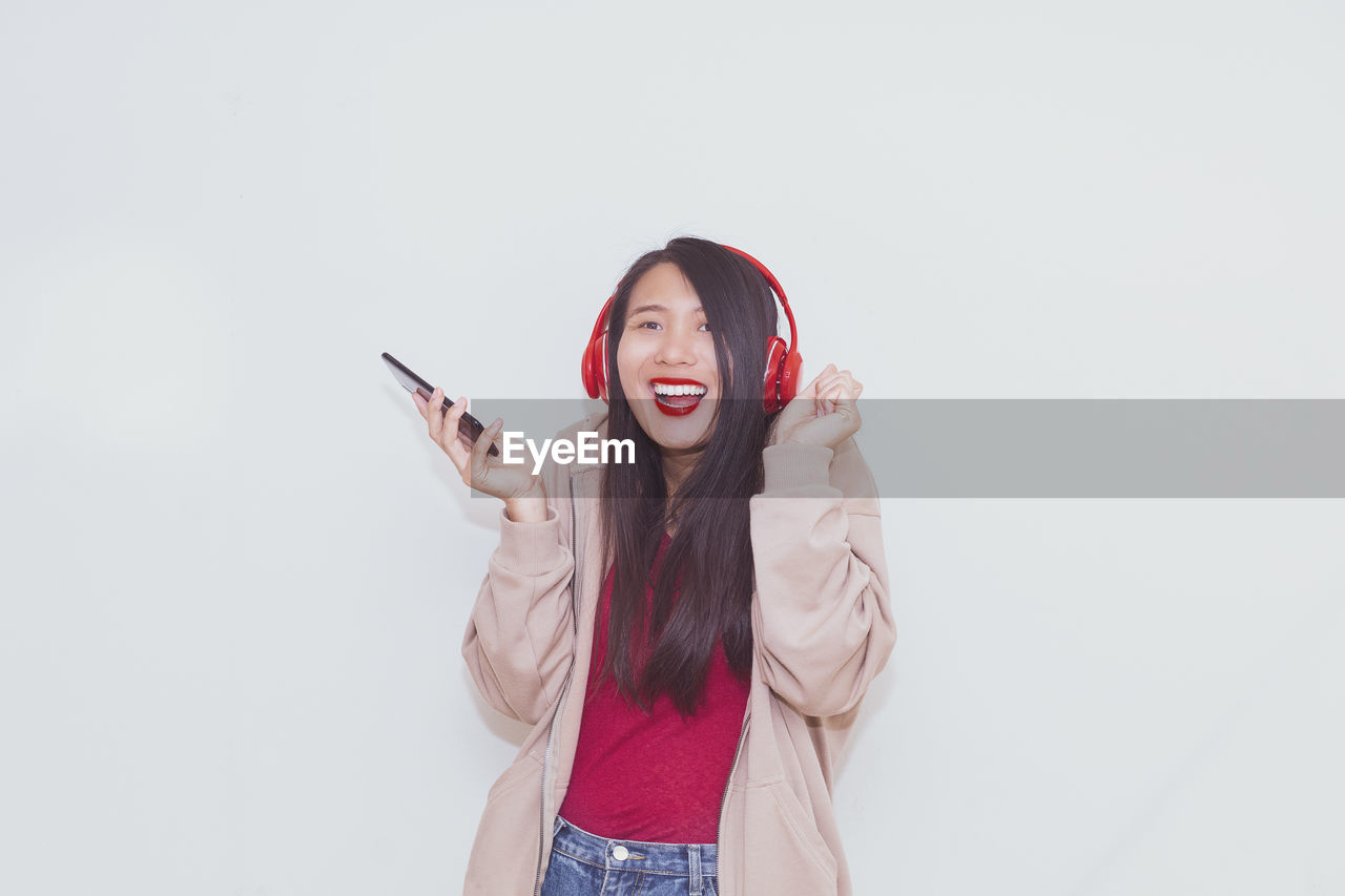 PORTRAIT OF YOUNG WOMAN USING PHONE AGAINST WHITE BACKGROUND