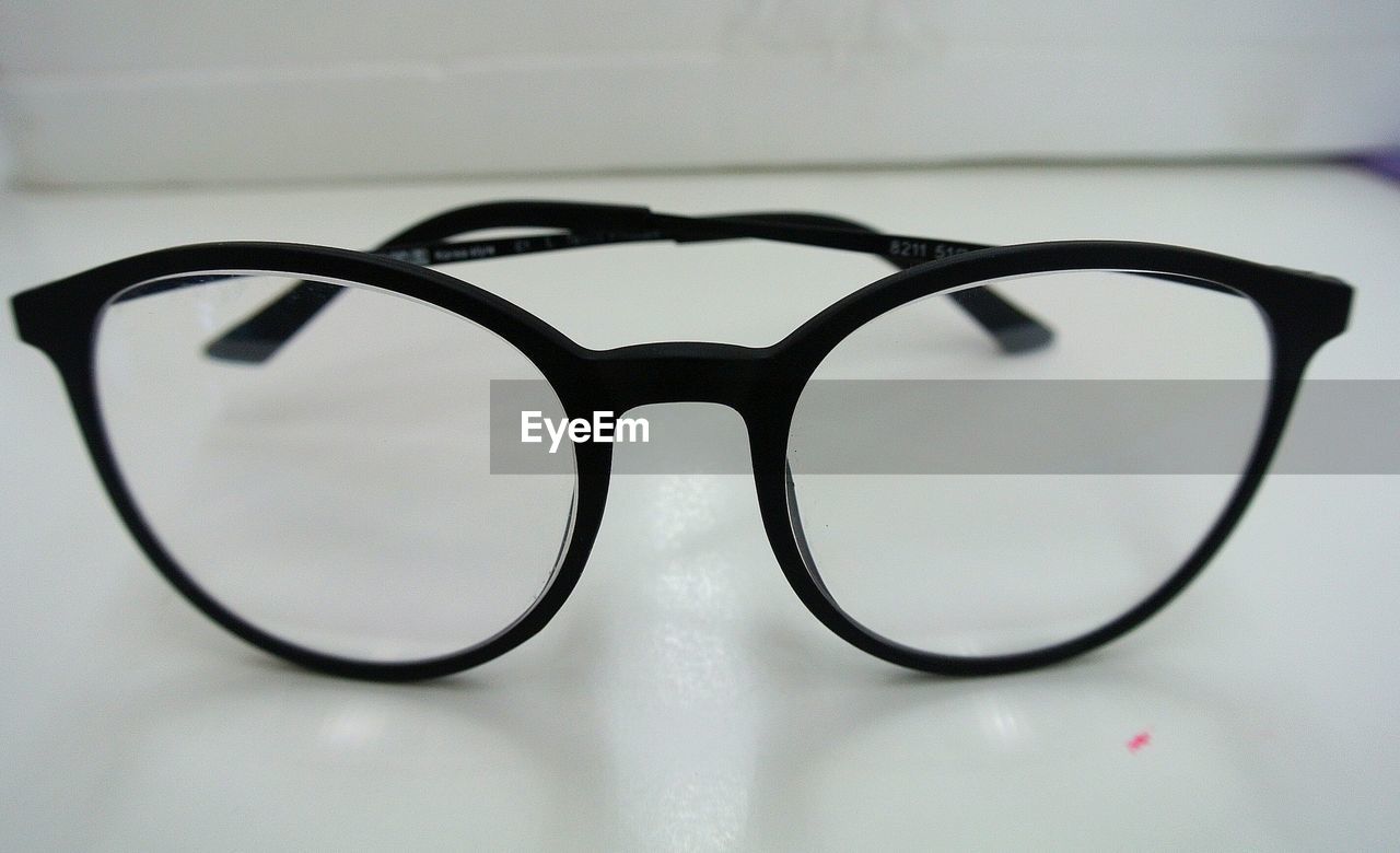 CLOSE-UP OF EYEGLASSES ON TABLE AGAINST WALL