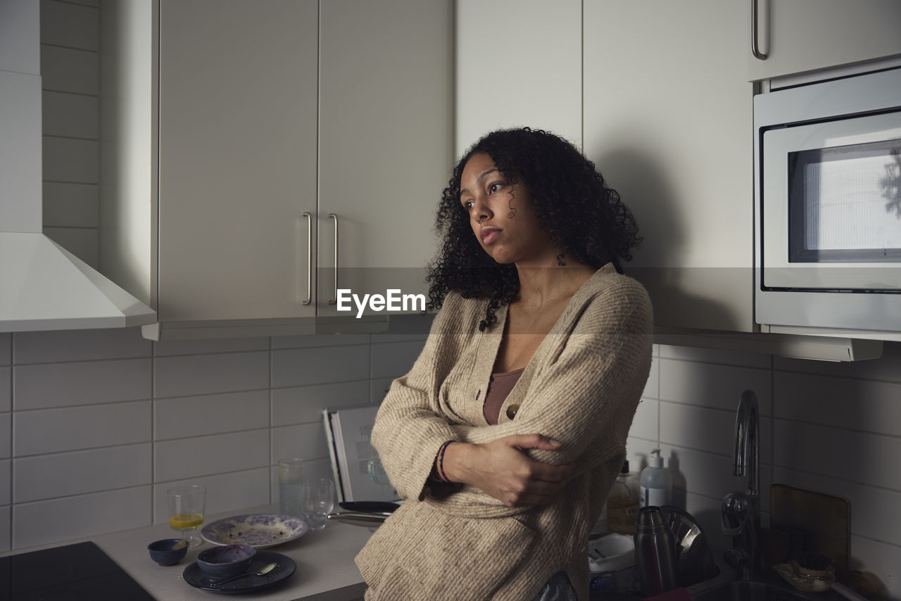 Pensive young woman standing in kitchen