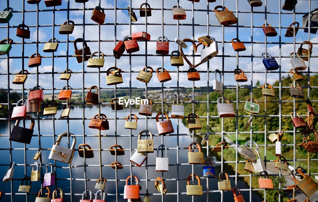 Full frame shot of padlocks hanging on fence against sky