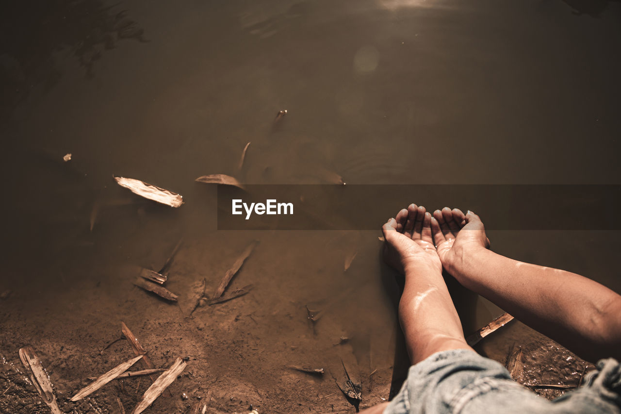 Cropped image of hands holding water over lake