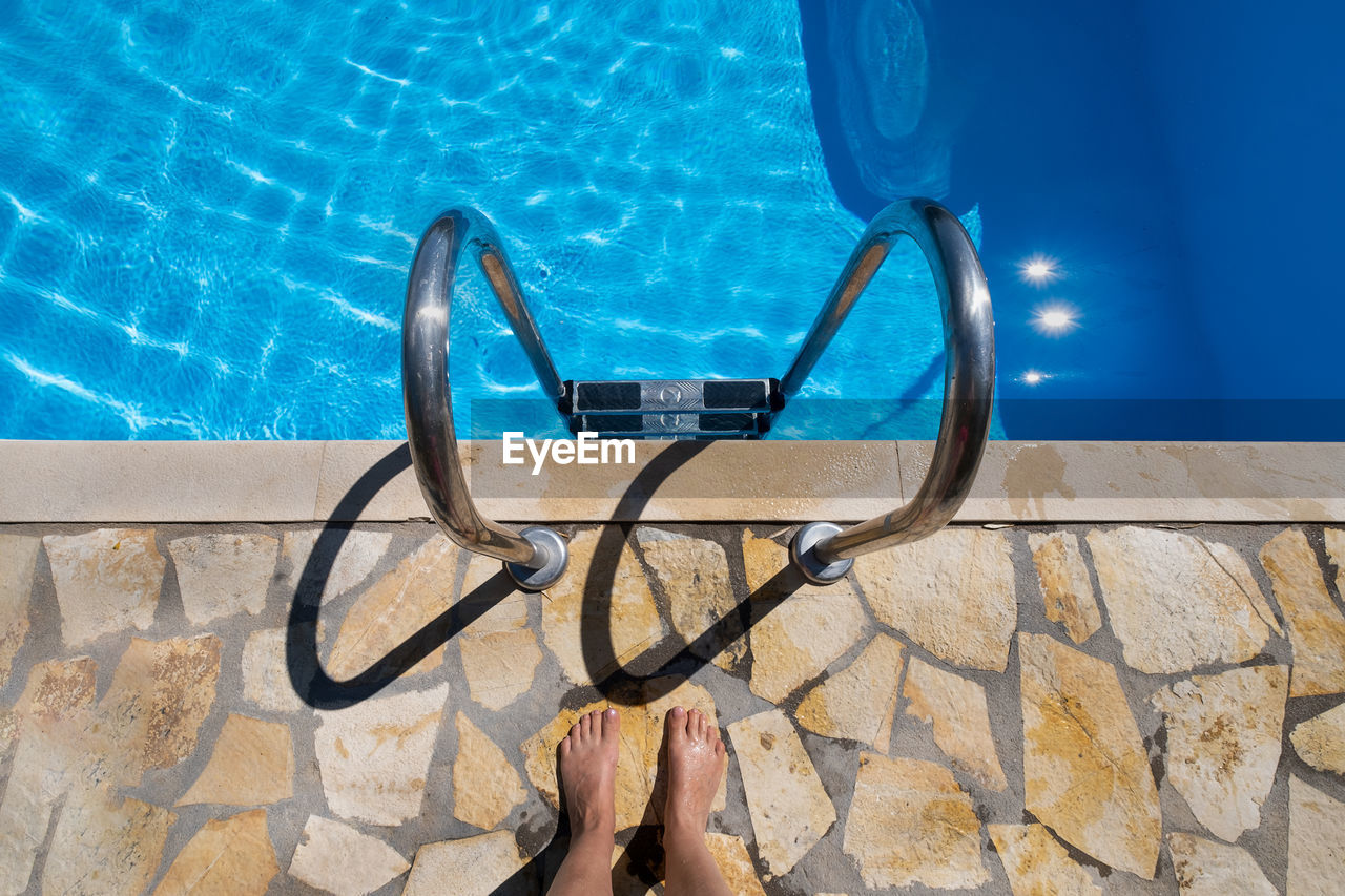 LOW SECTION OF WOMAN STANDING BY SWIMMING POOL