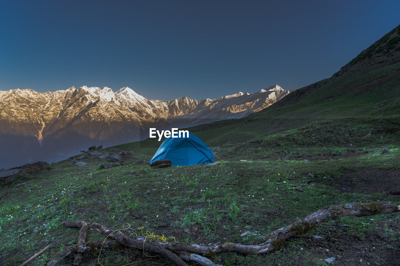 Tent on land by mountain against clear blue sky