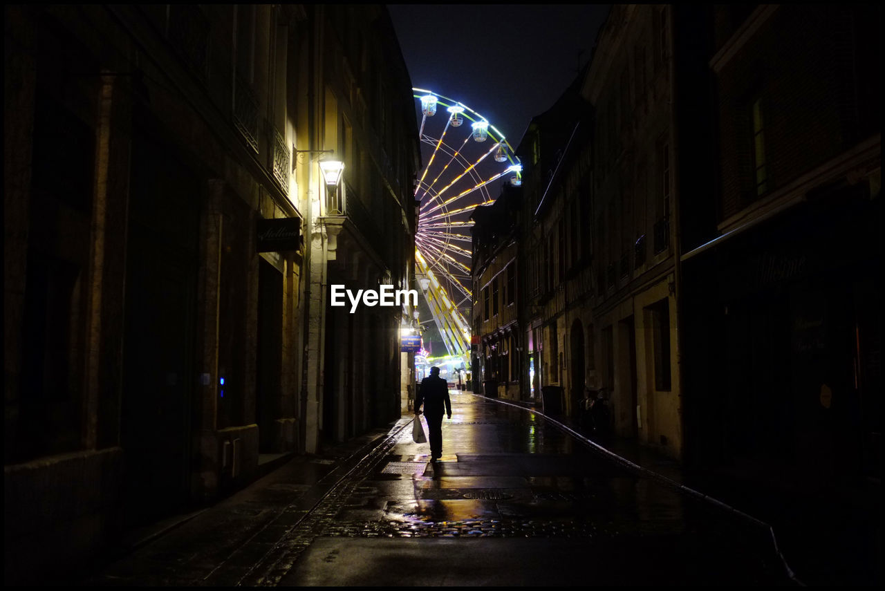 PEOPLE WALKING ON ILLUMINATED STREET IN CITY AT NIGHT