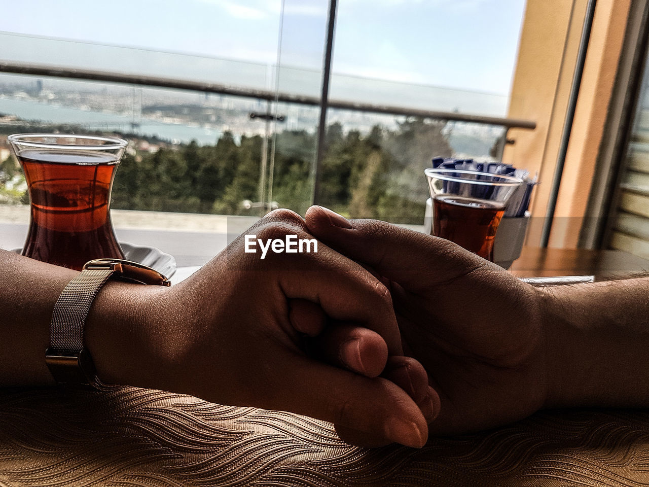 Close-up of couple holding hands on table against window