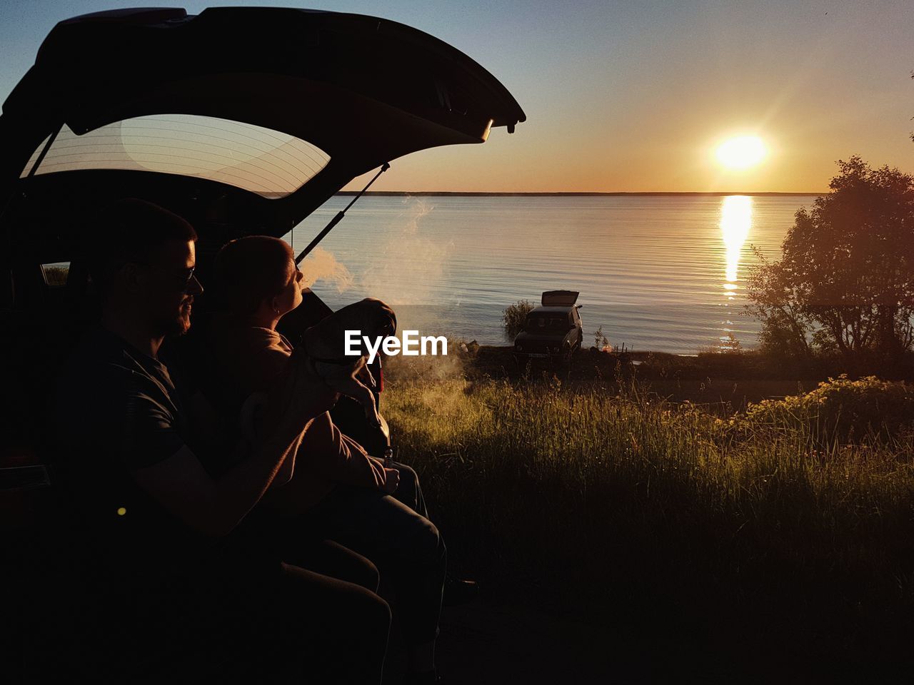 PEOPLE SITTING ON LAND AGAINST SKY DURING SUNSET