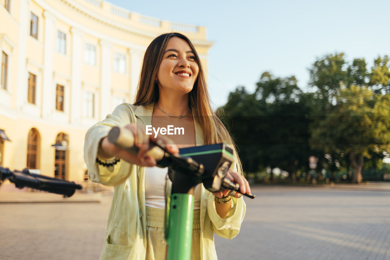 Smiling young woman with electric push scooter in city