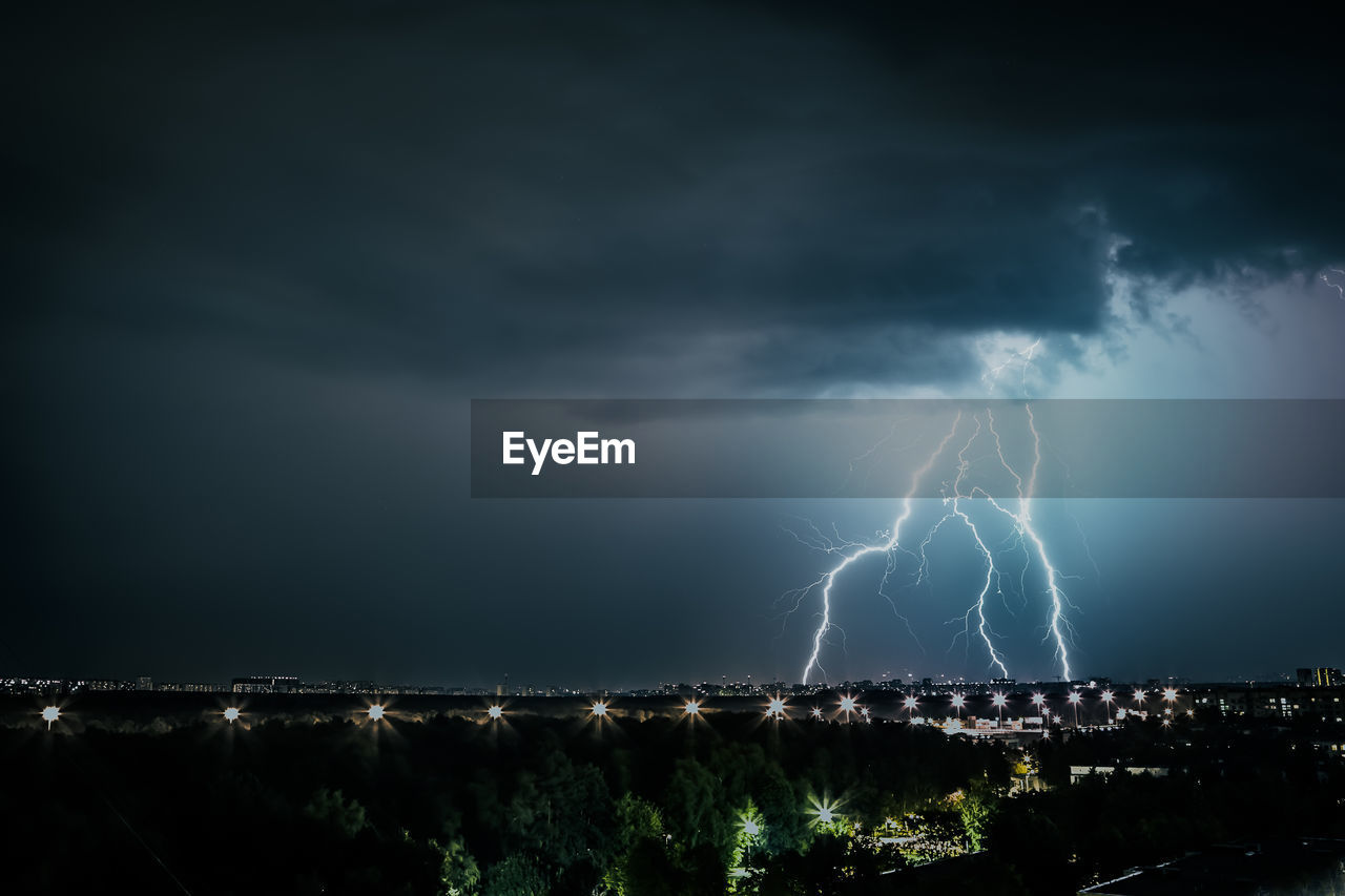 Lightning over illuminated cityscape against sky at night