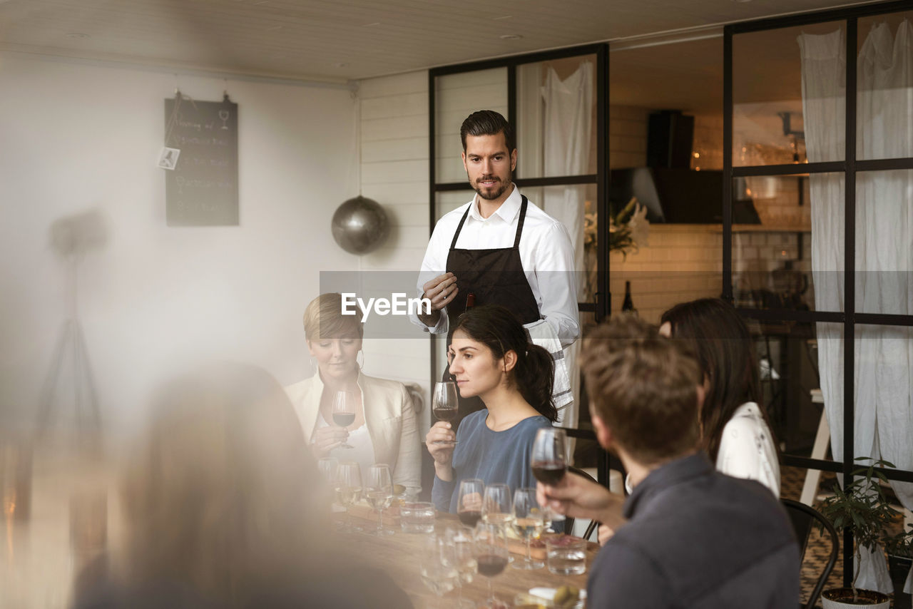 Man wearing apron looking at people tasting wine at workshop