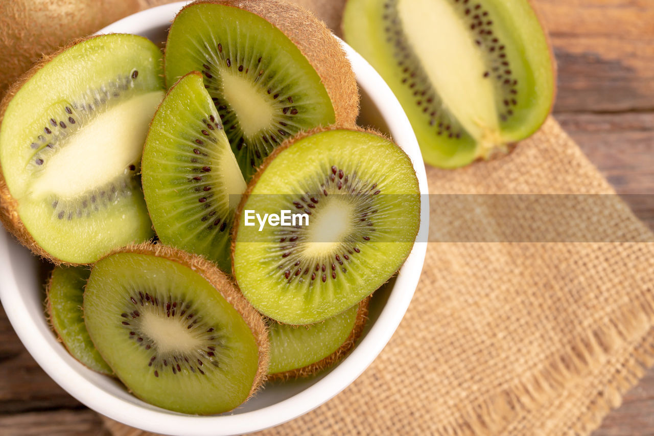 Top view fresh green kiwis slice in the white bowl on the old wooden table