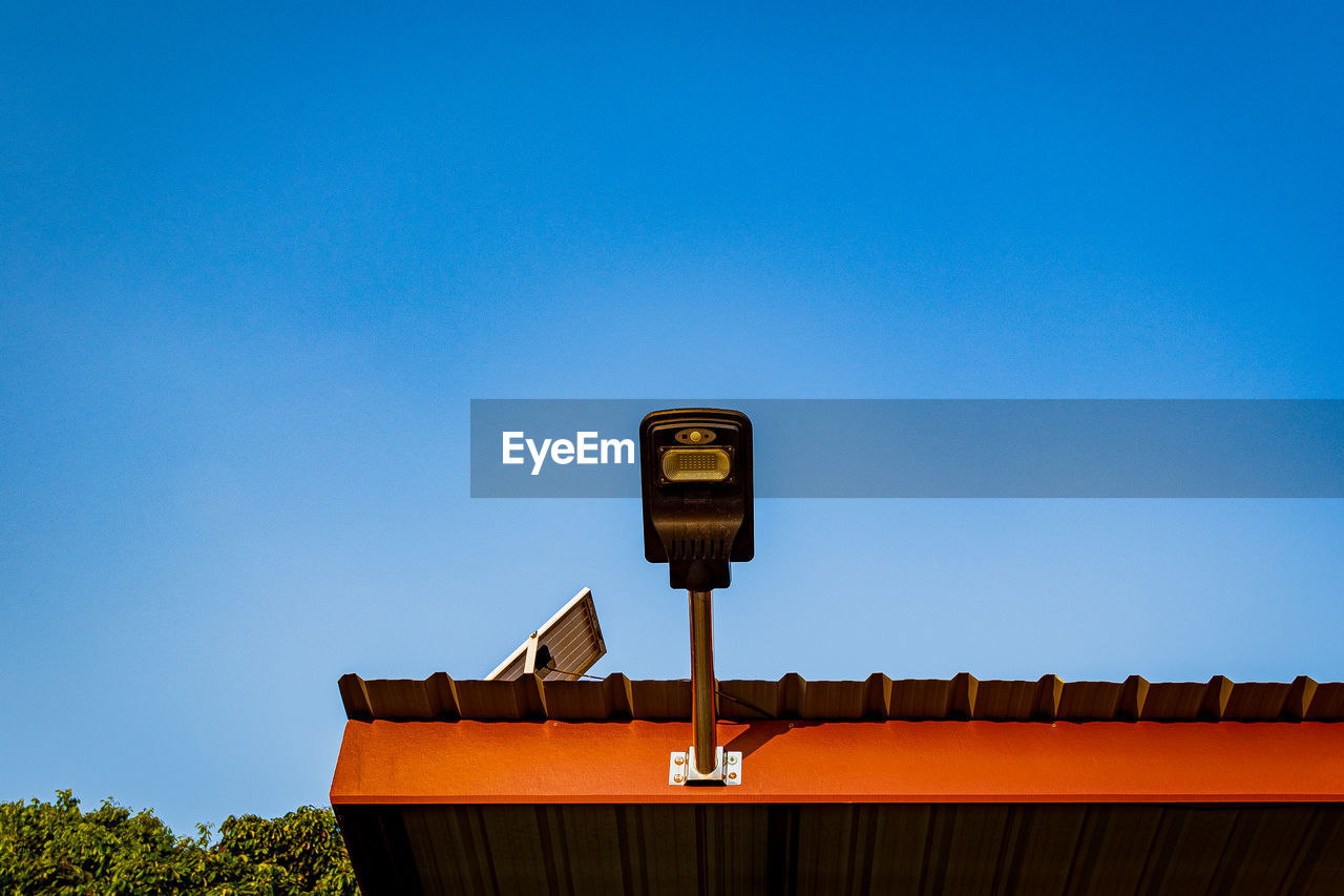 Low angle view of security camera against clear blue sky