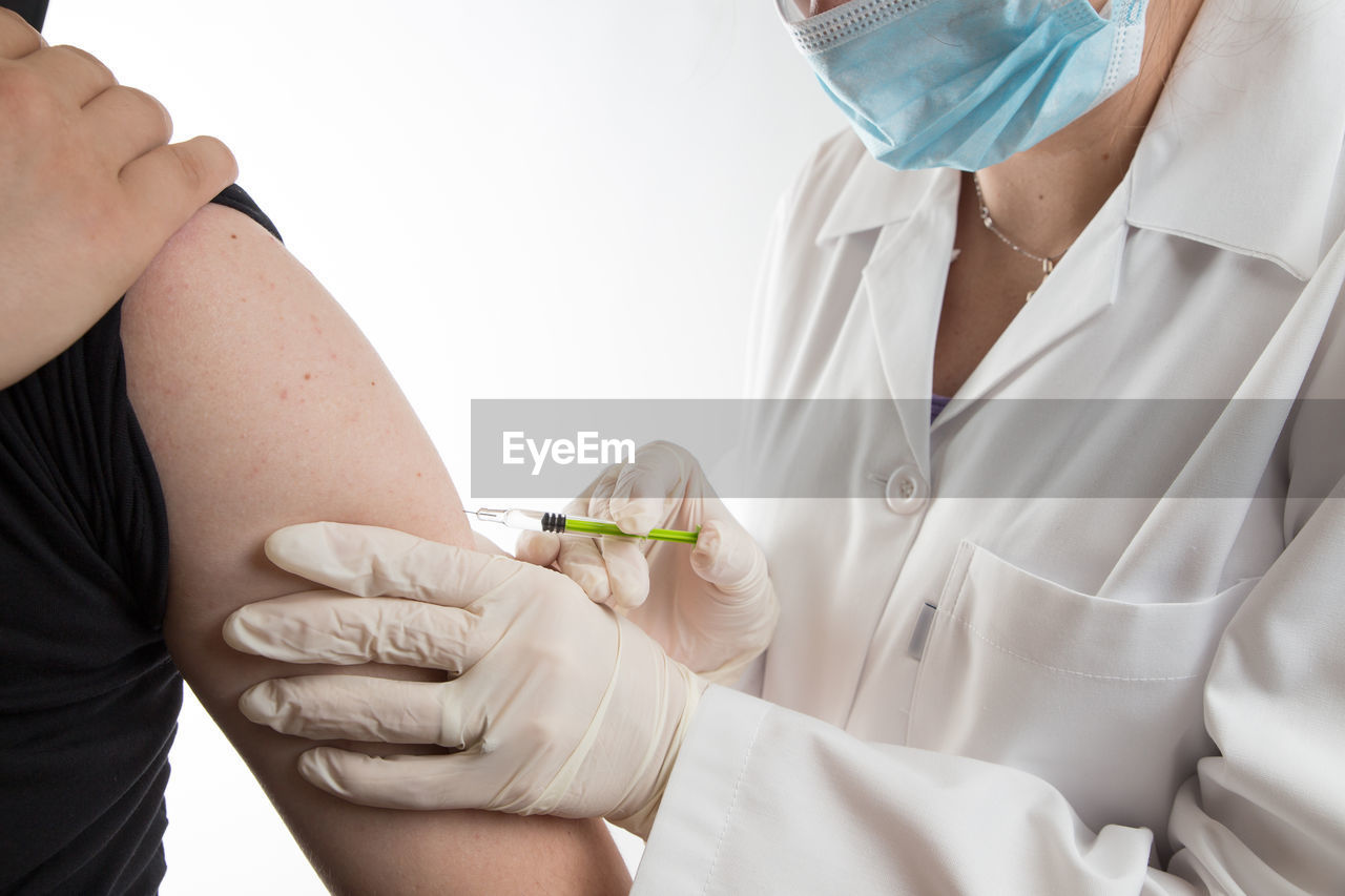 Midsection of doctor injecting syringe to patient against white background