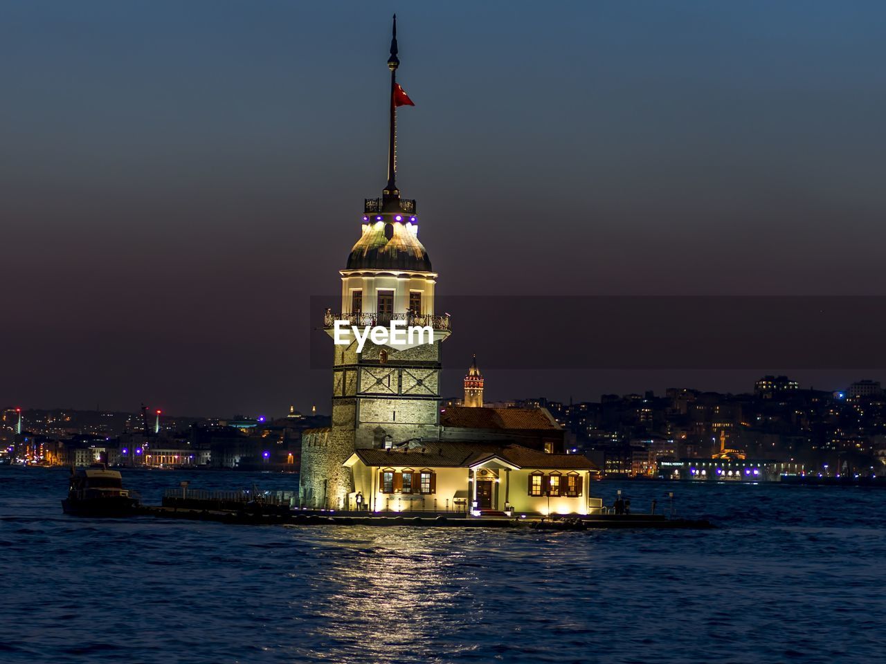 Illuminated building by sea against sky at night