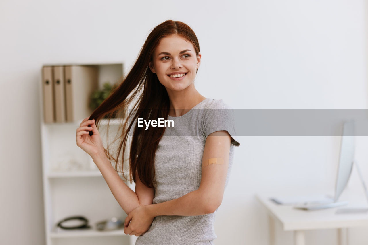 PORTRAIT OF SMILING WOMAN STANDING AGAINST WALL AT HOME