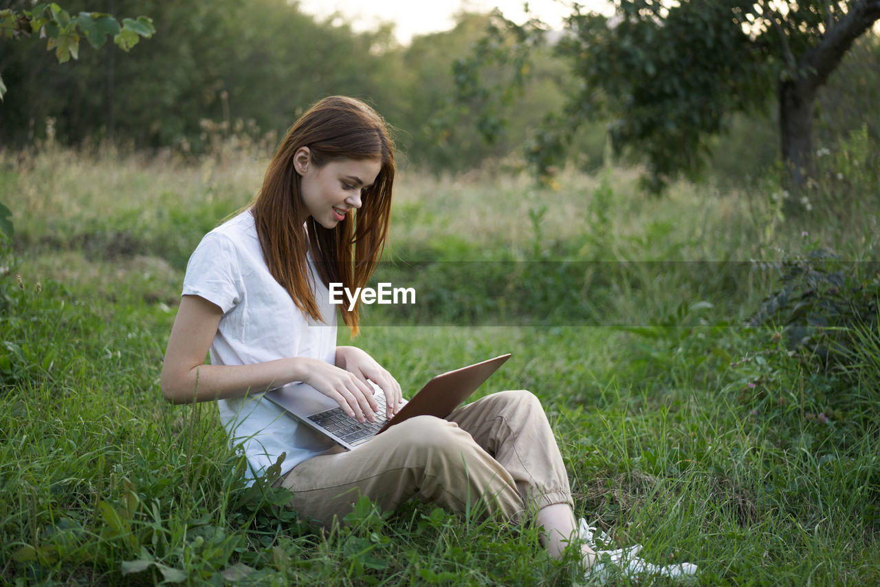 portrait of young woman using laptop while sitting on field