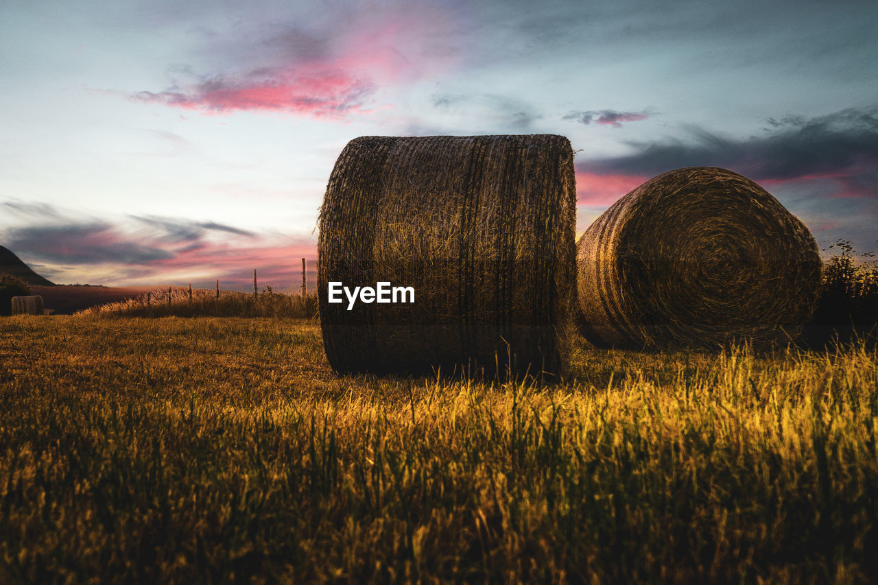 HAY BALES IN FIELD AGAINST SKY DURING SUNSET