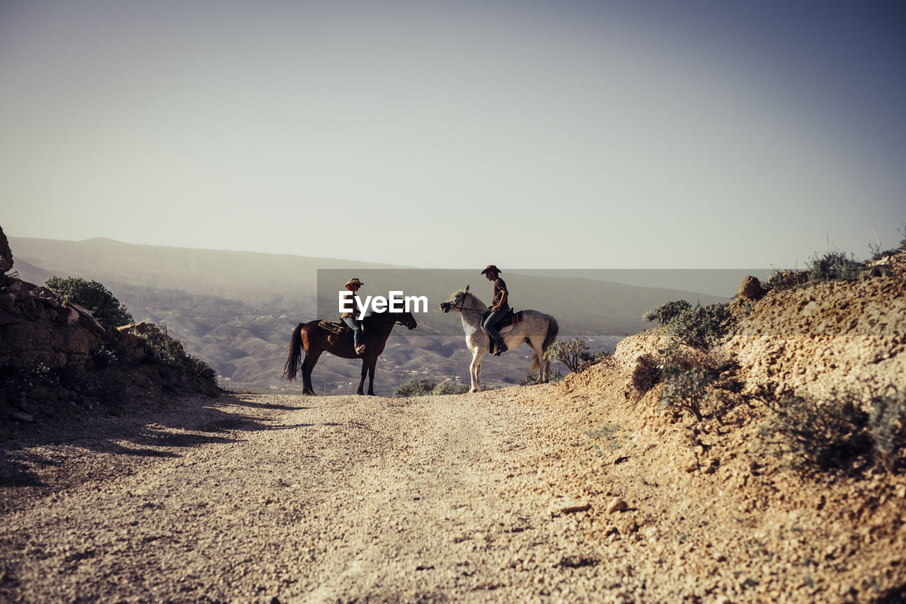 People riding horses on landscape against sky