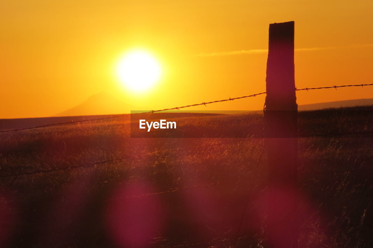 Sunlight falling on fence at field during sunset