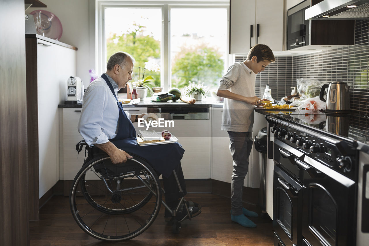 Son with disabled father cutting vegetables in kitchen