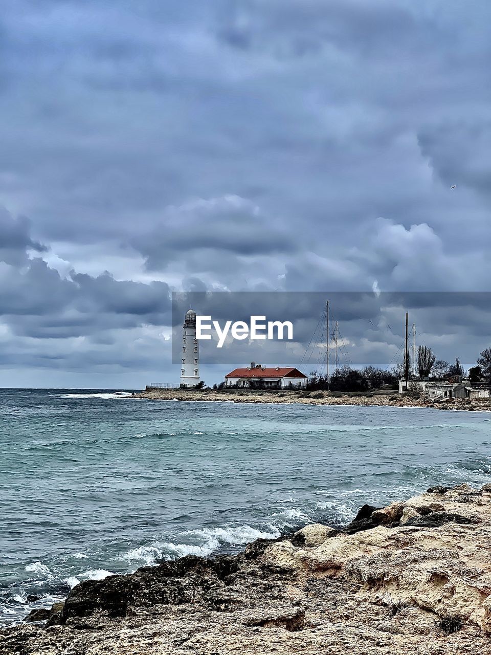 LIGHTHOUSE AMIDST SEA AND BUILDINGS AGAINST SKY