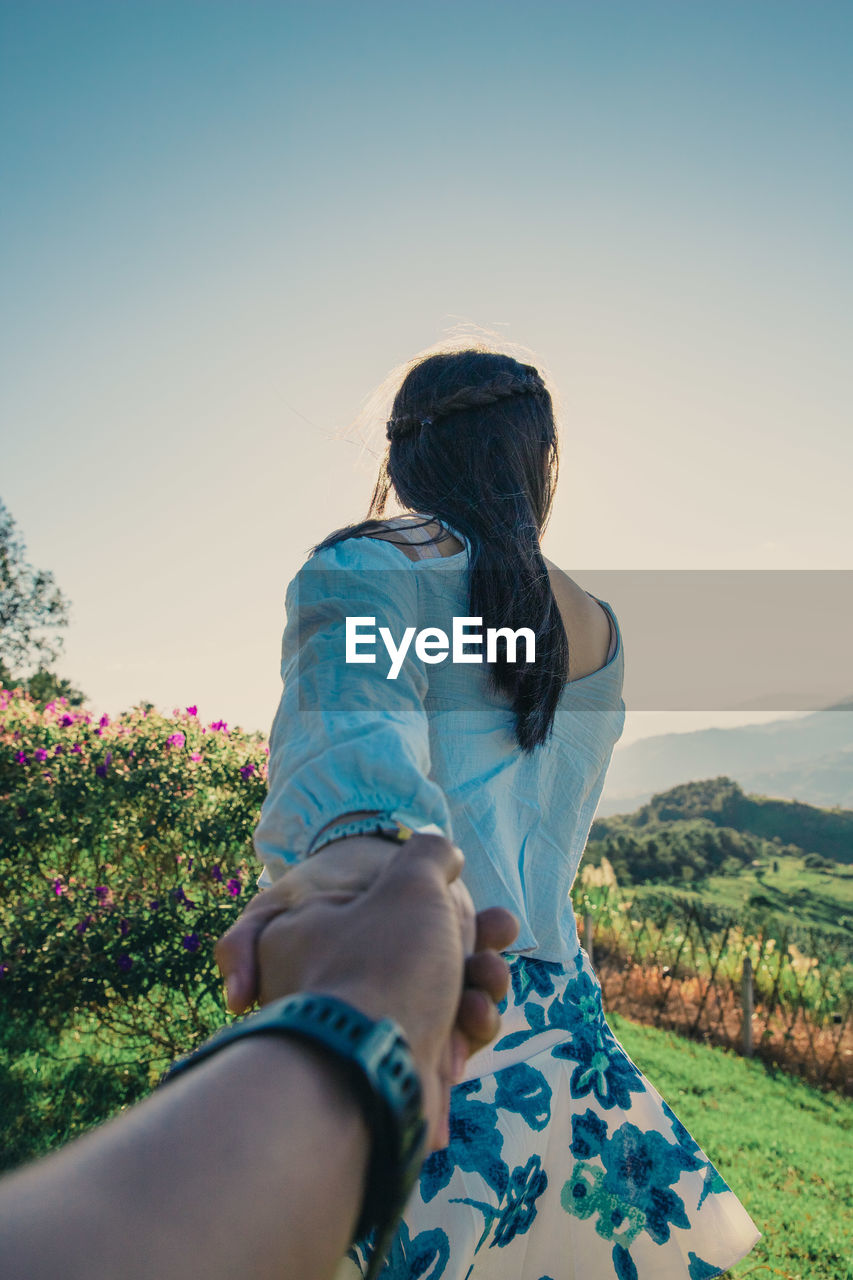 Woman holding cropped hand against clear sky