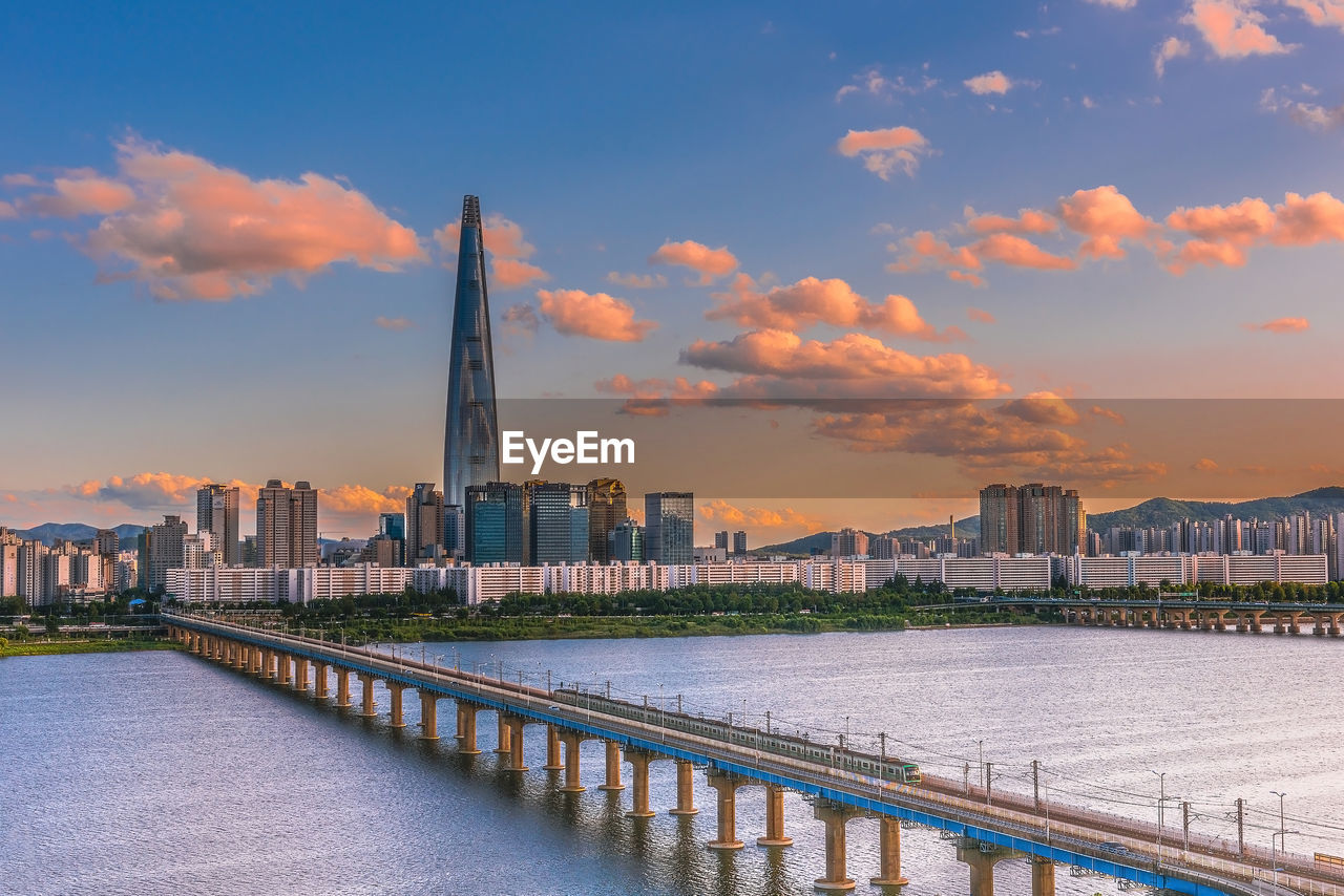 Bridge over river by buildings against sky during sunset