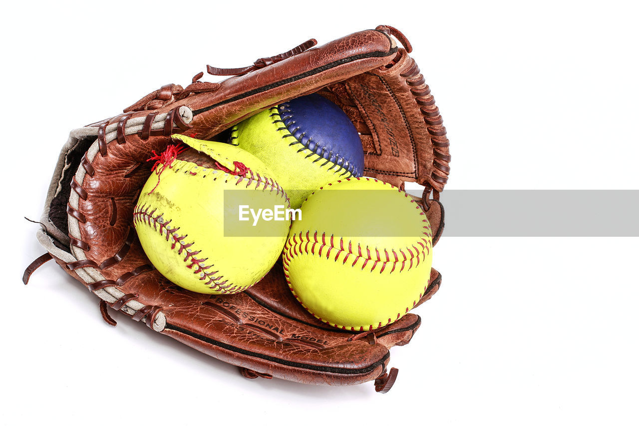 Close-up of baseball glove and balls against white background