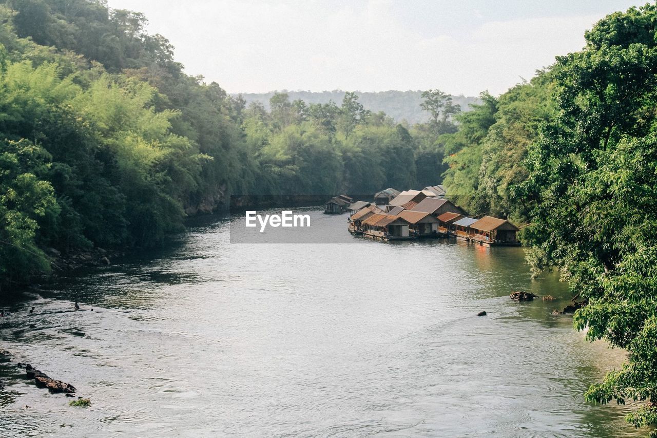 Stilt houses by river amidst trees against sky