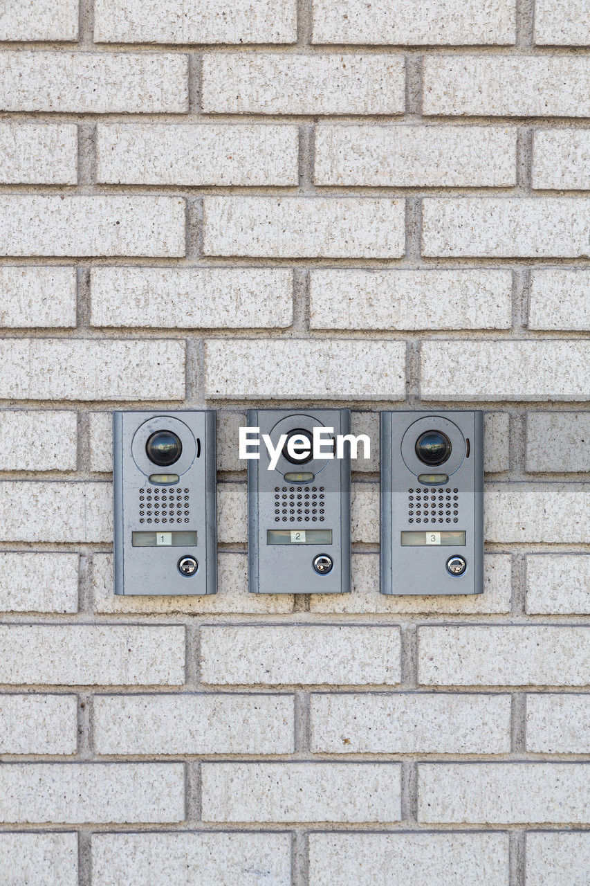 Three intercom on white textured brick wall, close up