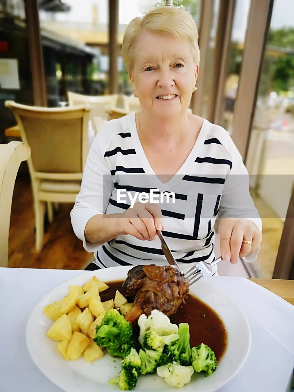 food and drink, food, one person, lunch, smiling, meal, portrait, child, happiness, front view, childhood, dish, looking at camera, blond hair, emotion, women, eating, table, indoors, vegetable, plate, healthy eating, female, restaurant, waist up, business, lifestyles, holding, casual clothing, brunch, cheerful, striped, wellbeing, cook, freshness, adult, domestic life, chair, person, sitting, enjoyment, day, domestic room, apron