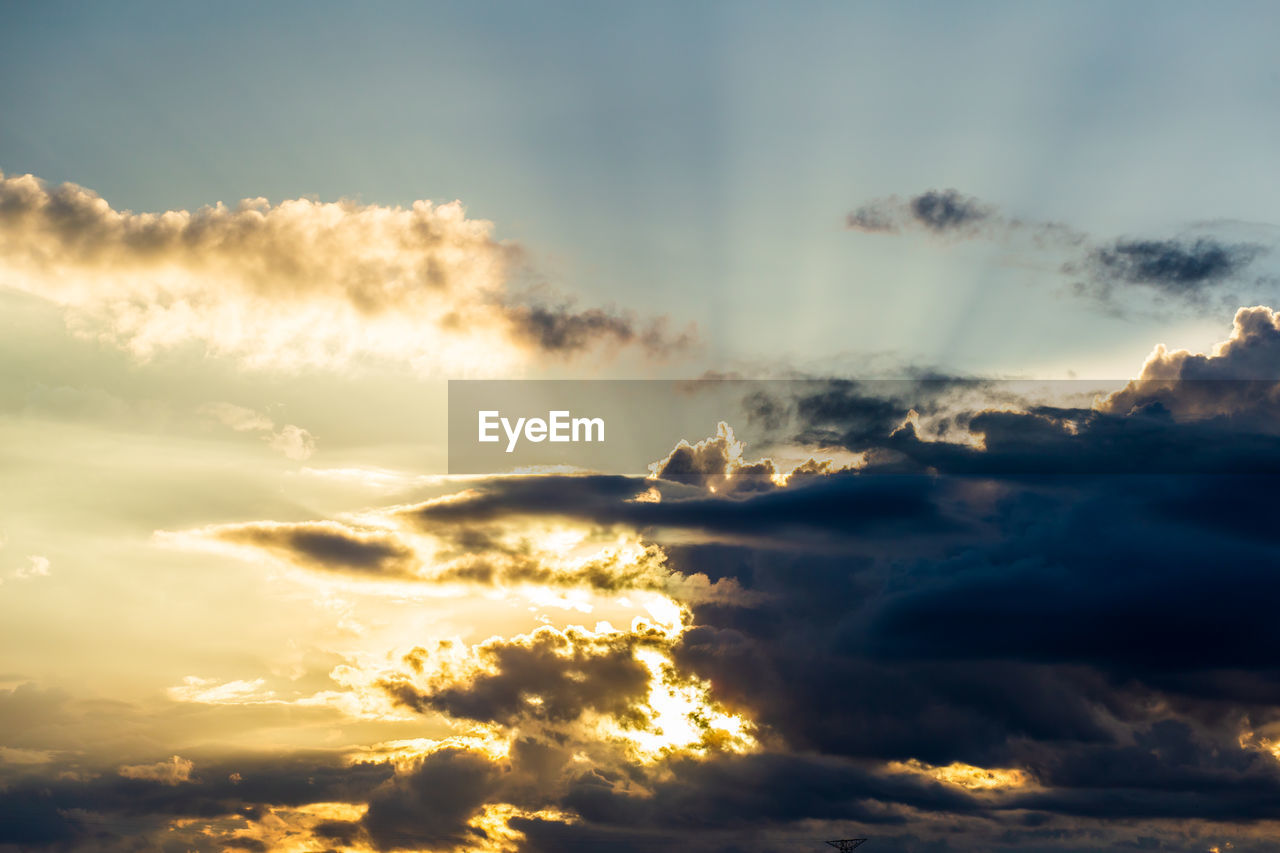 Low angle view of sunlight streaming through clouds during sunset