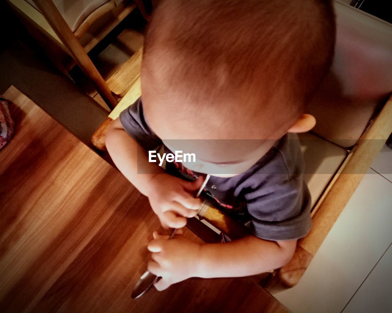 HIGH ANGLE VIEW OF BABY BOY HOLDING HARDWOOD AT HOME