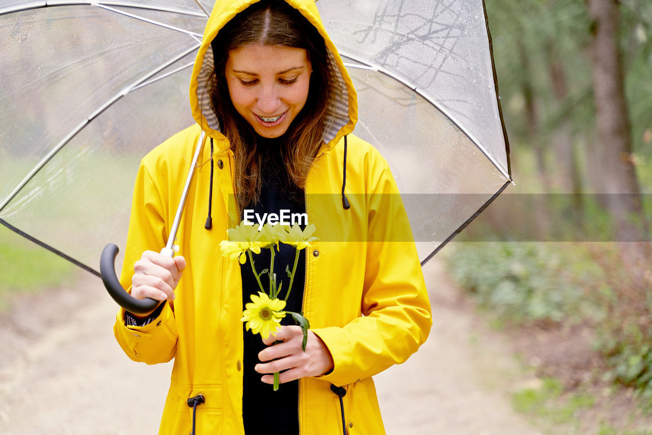 Smiling woman holding flower during rain