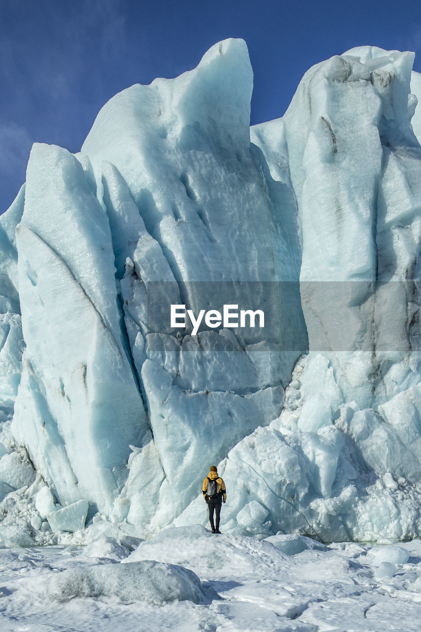 Back view of unrecognizable traveler hiker admiring spectacular scenery of frozen seashore with ice and snow in winter in iceland